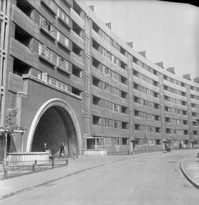 A Black and white photo of curve-fronted 6 story building with and archway into the social housing complex
