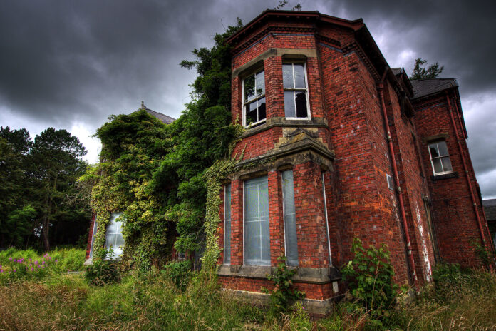 A truly ugly overgrown, abandoned mental hospital under a gloomy sky.