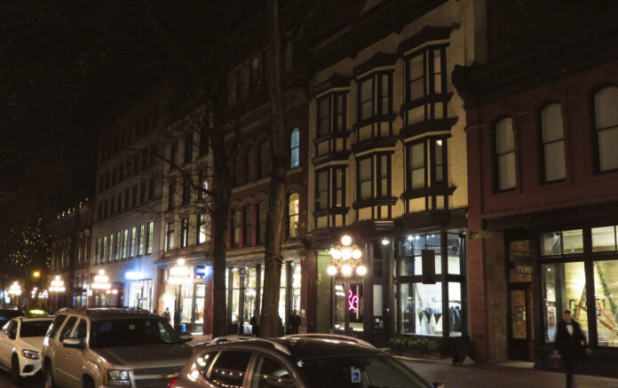 a row of older buildings at night, the storefront below residents appear prosperous.